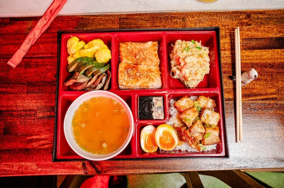 A Bareo bento box with salmon, pork belly rice, soft egg and pickled vegetables