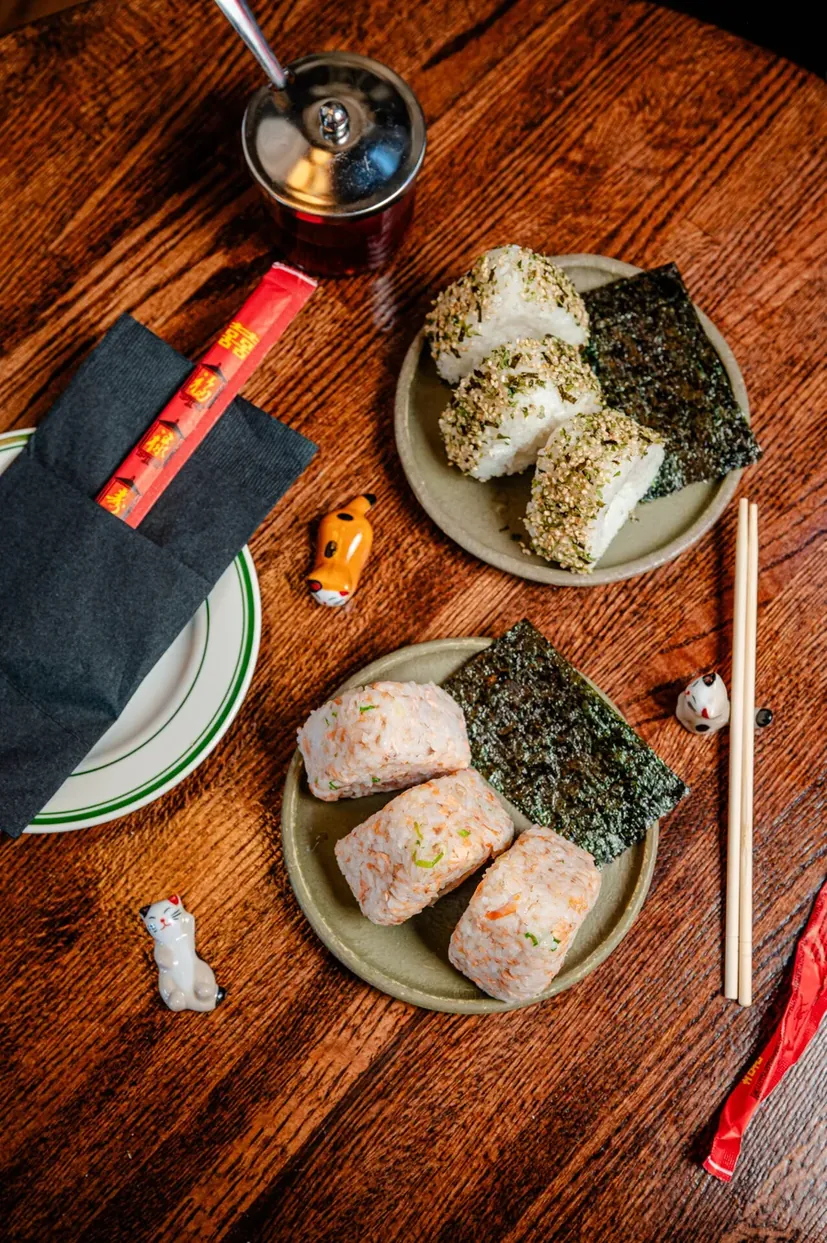 Plates of onigiri with chopsticks on a wood table at Bareo