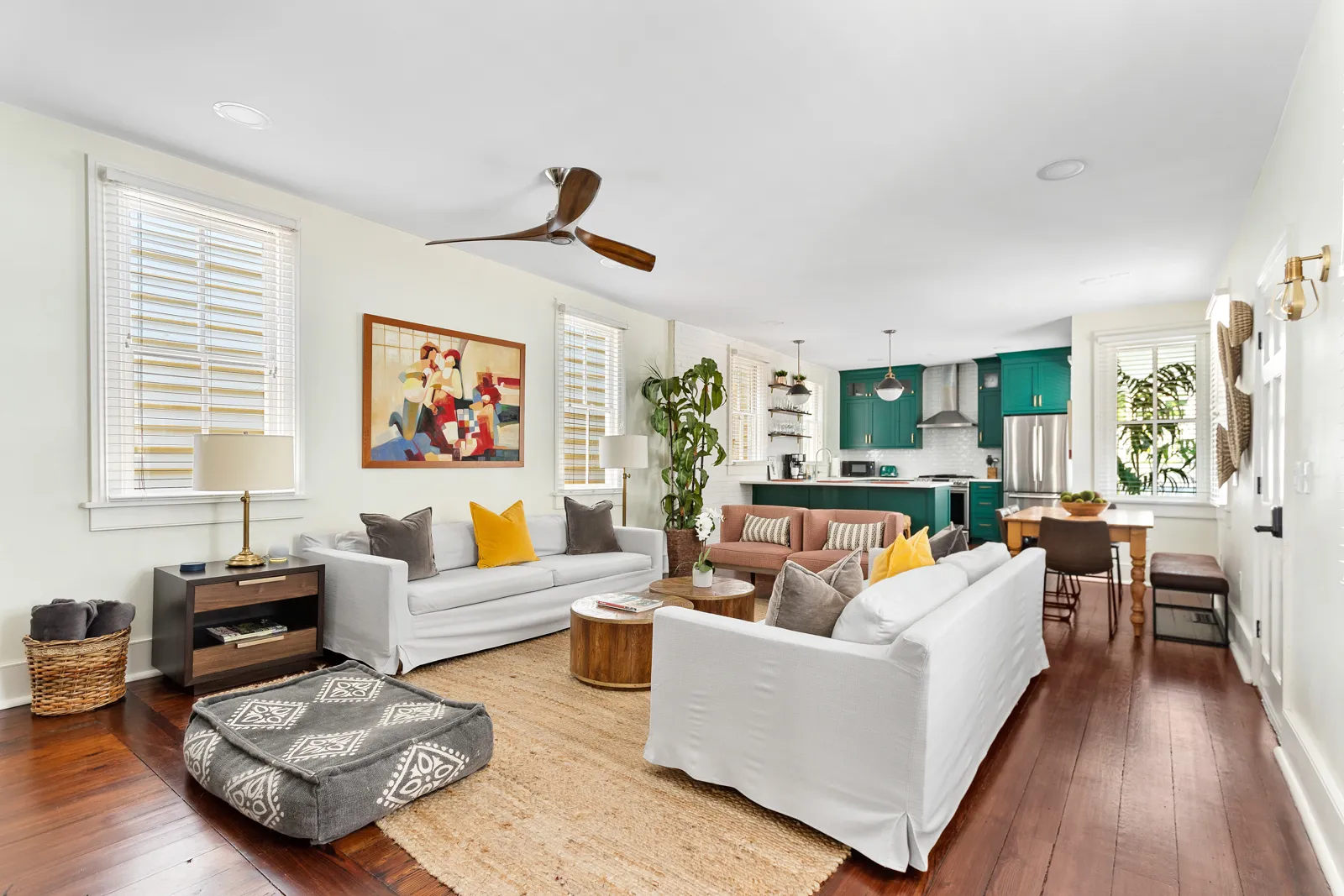 The Mint Julep living room with twin white sofas under a ceiling fan, open to the julep green kitchen