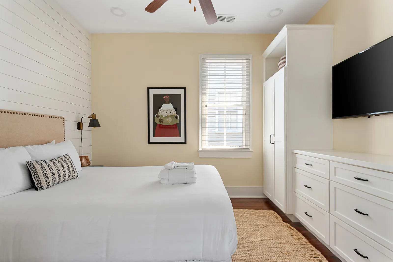 A bedroom with a wall of built-in white dressers and a TV