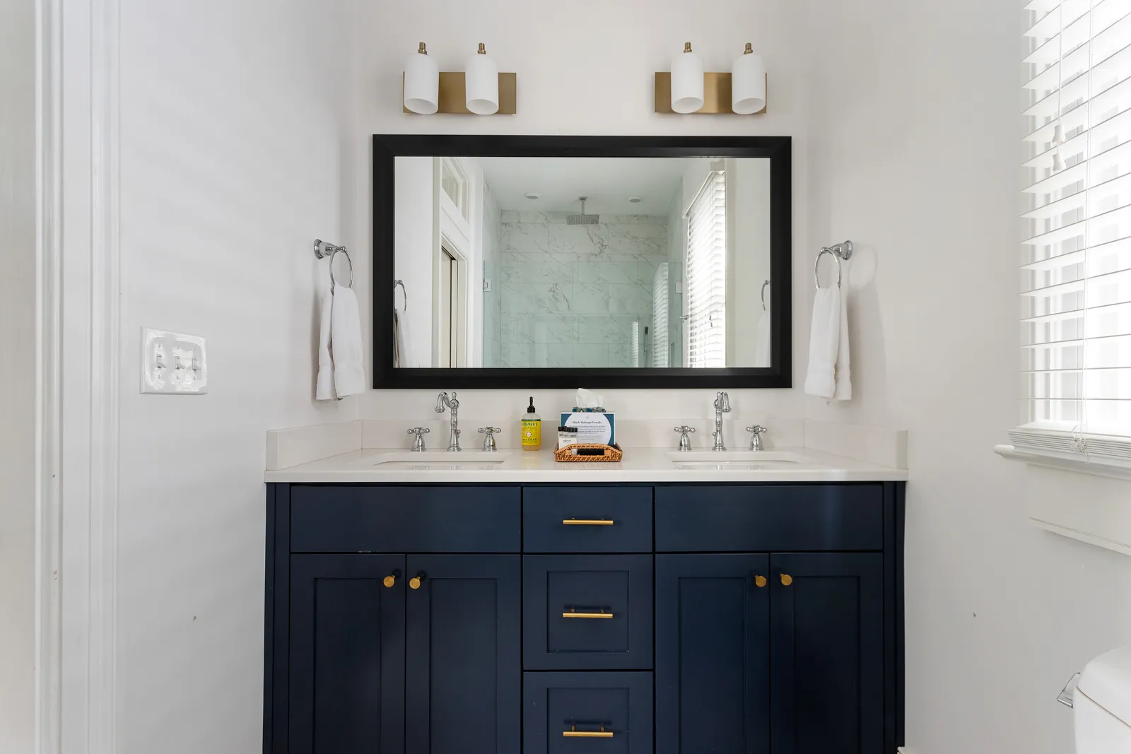 A full bathroom with a navy double vanity and black-framed mirror