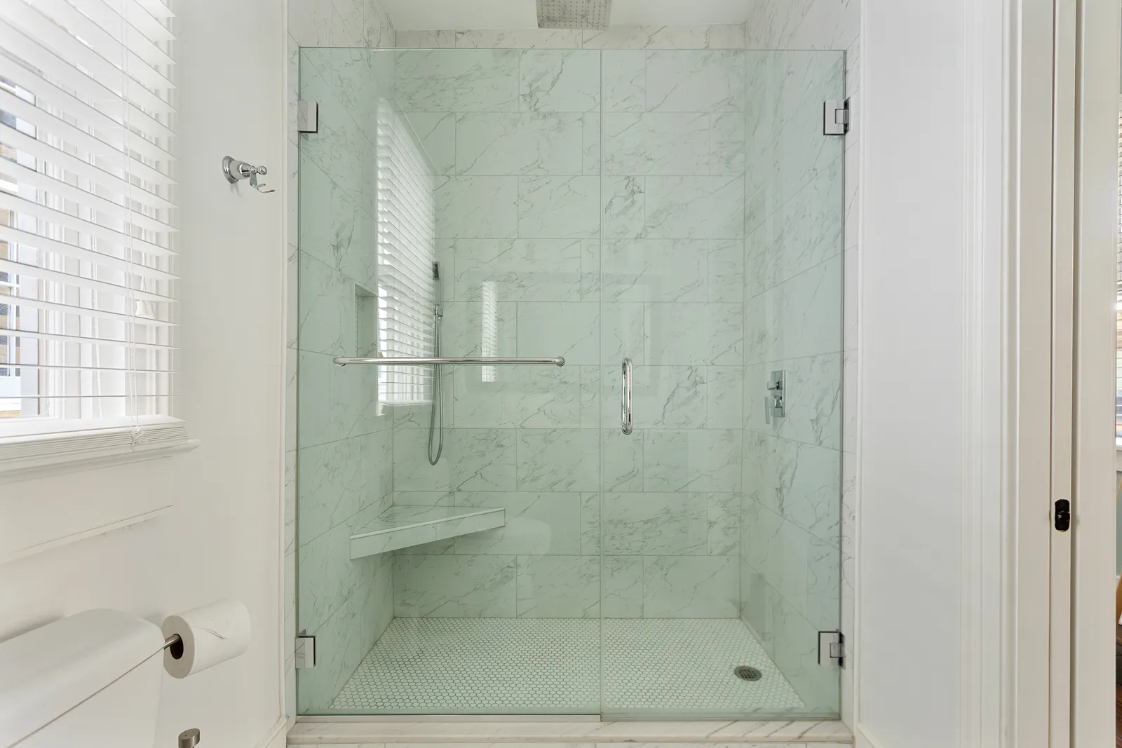 A glass walk-in shower in white marble-look tile