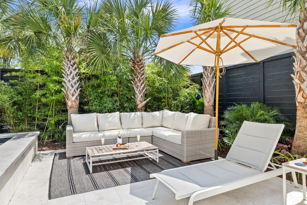 The poolside lounge with a wicker sectional under an umbrella and palms