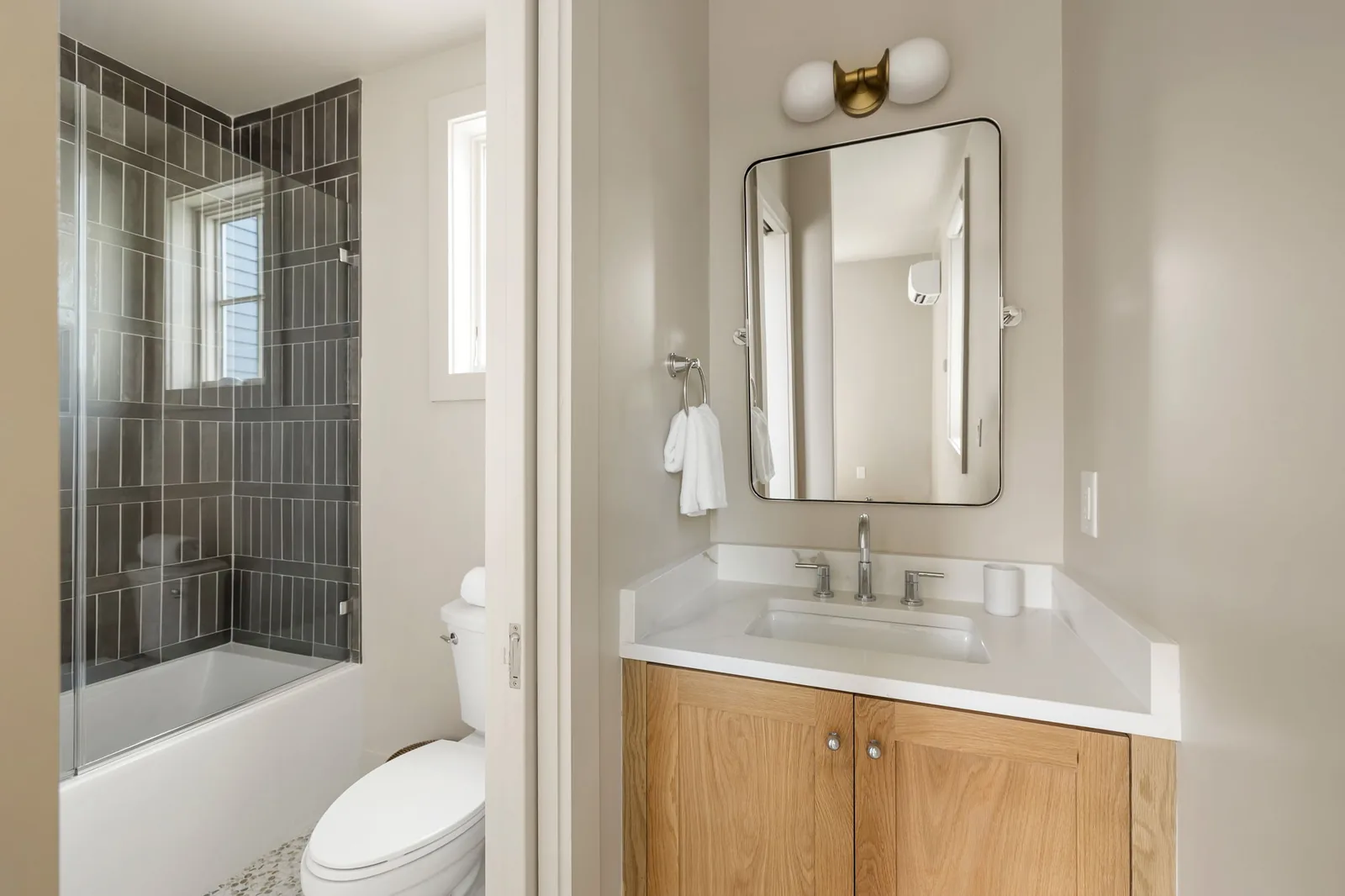 The sister residence's ensuite vanity in white oak beside the dark glazed tub