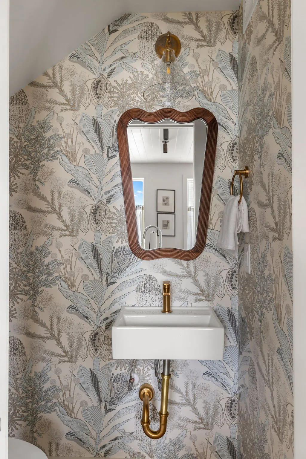 A powder room with botanical wallpaper, brass fixtures and a sculpted wood mirror
