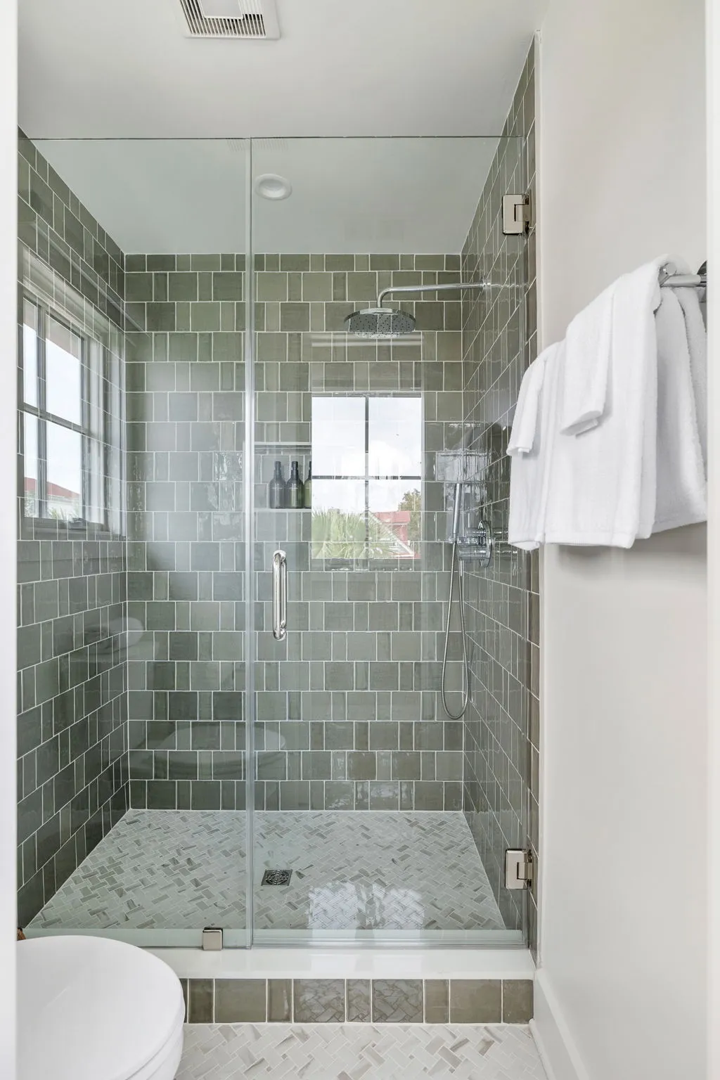 A walk-in shower in sage green tile with a rainfall head