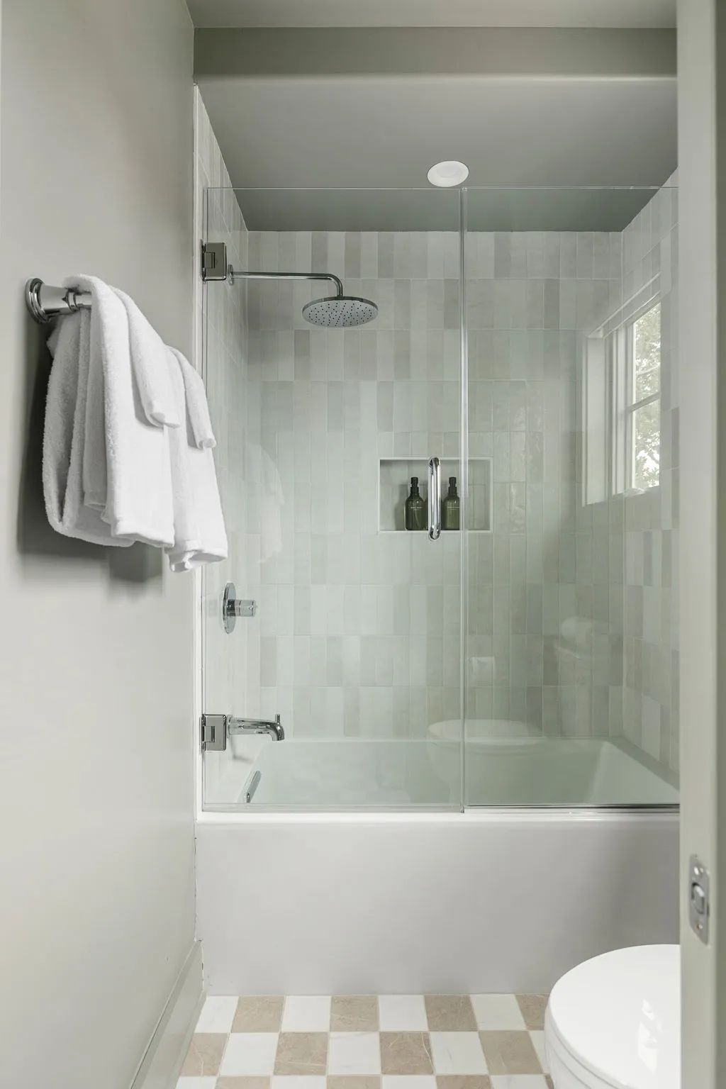 An ensuite bathroom with a rainfall shower over the tub in pale sage tile
