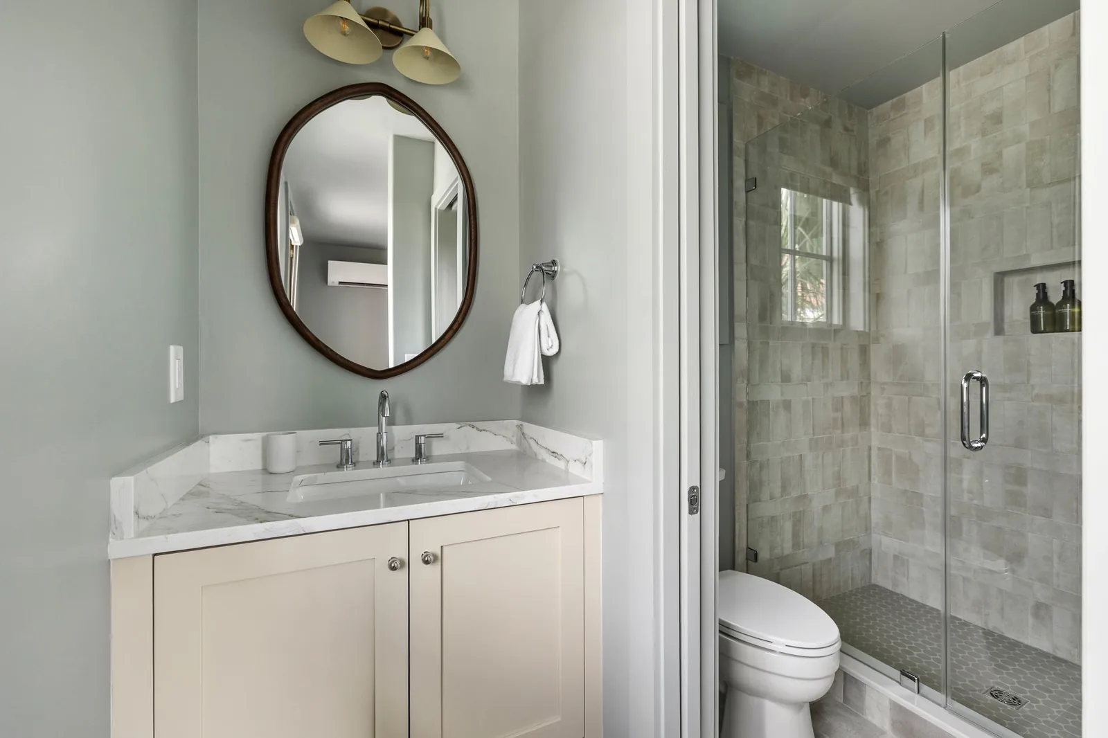 An ensuite vanity in cream with a marble counter, sculpted mirror and glazed shower beyond